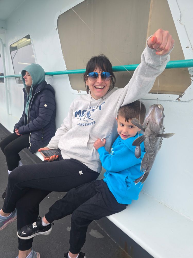 Woman and child smiling with caught fish on a boat.
