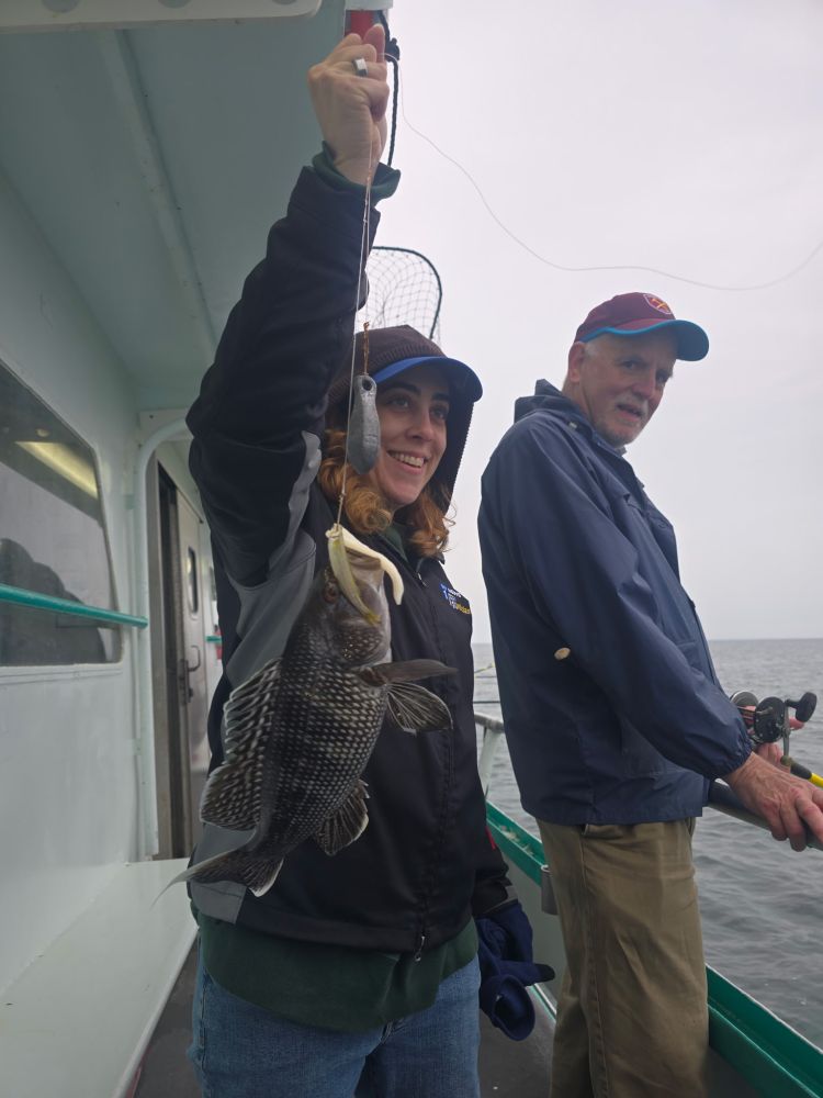 Person holding a fish on a boat beside another standing person.