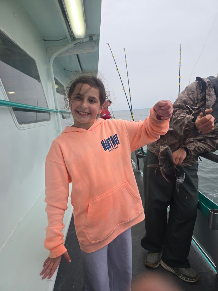 Smiling child in orange hoodie on boat holding a small fish.
