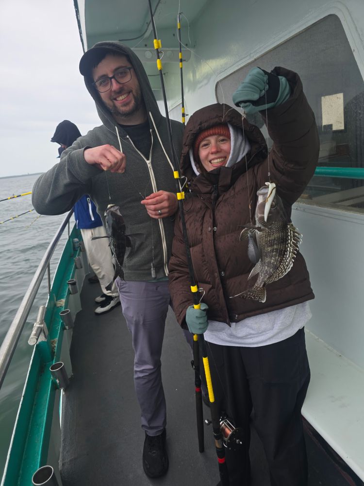 Two people on a boat holding freshly caught fish, smiling.