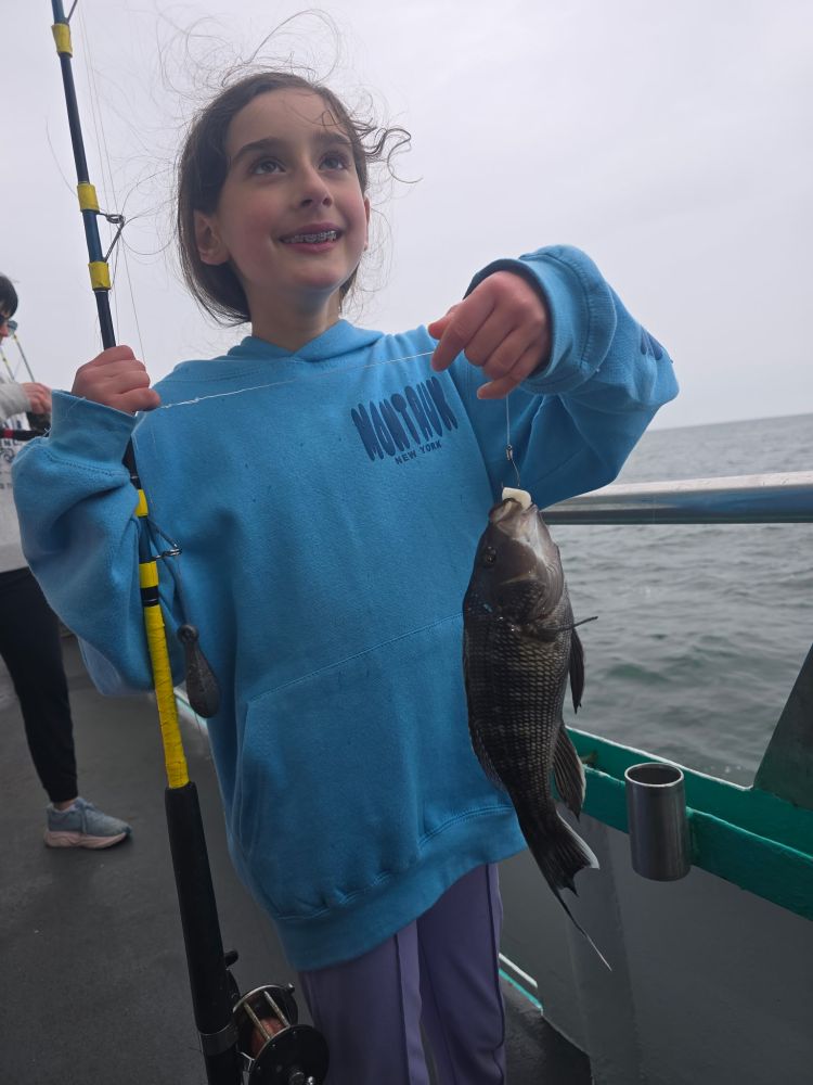 Child in blue hoodie holding fishing rod with a fish on a boat.