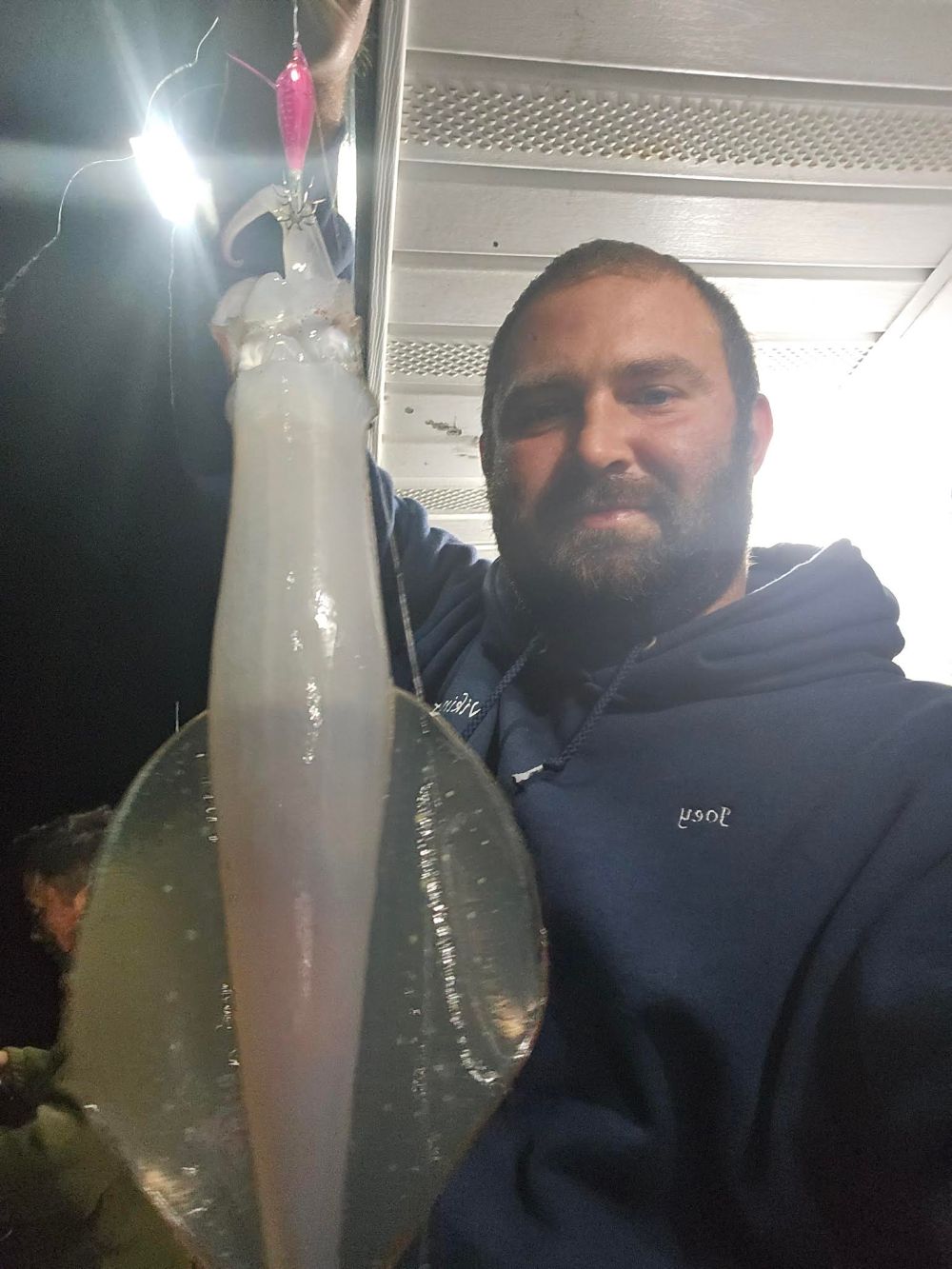 Man holding a large squid on a boat at night.