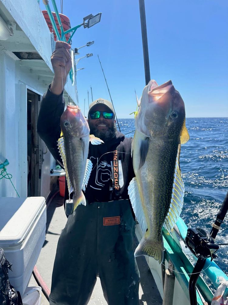 Man holding two large fish on a boat on a sunny day.