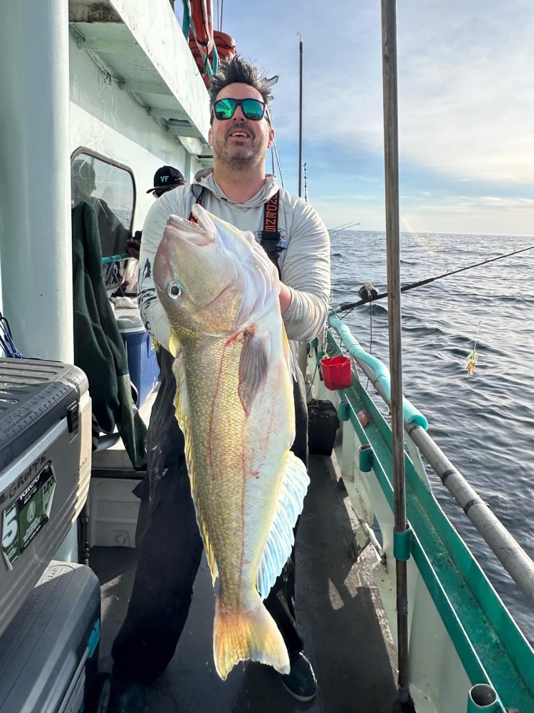Man on boat holds large fish with ocean in background.