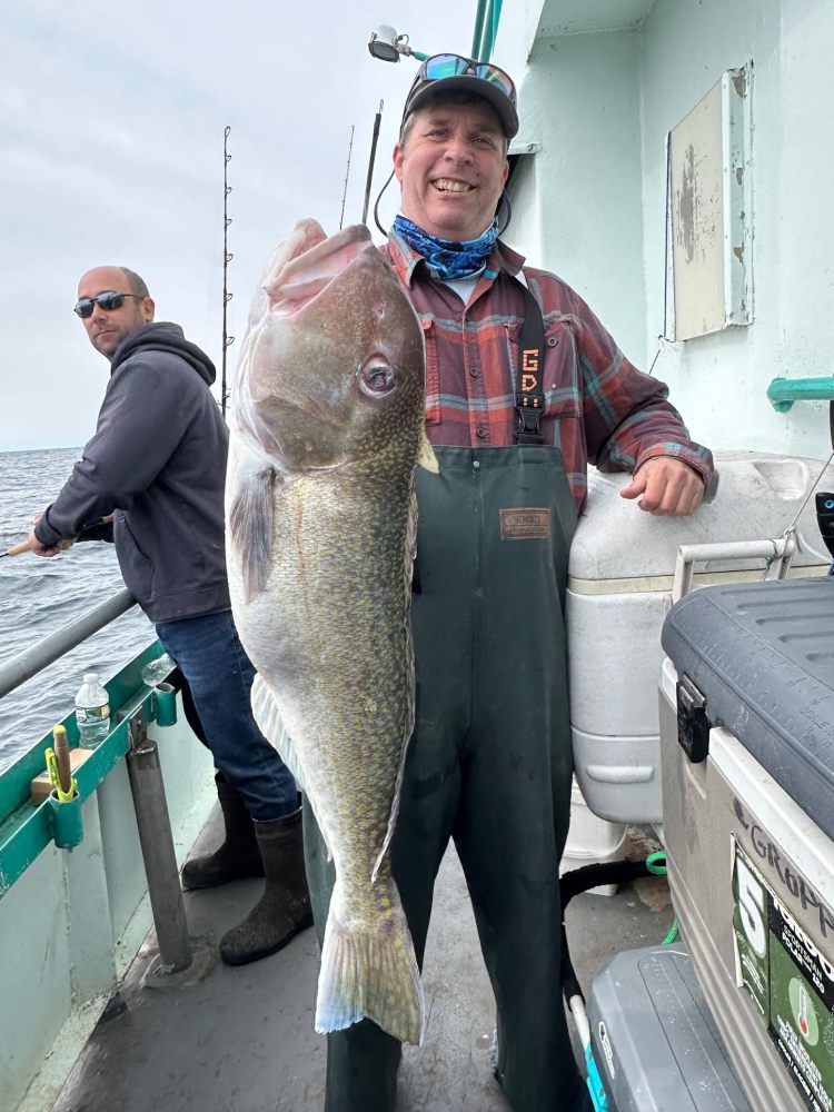 Two men on a boat, one holds a large fish and smiles.