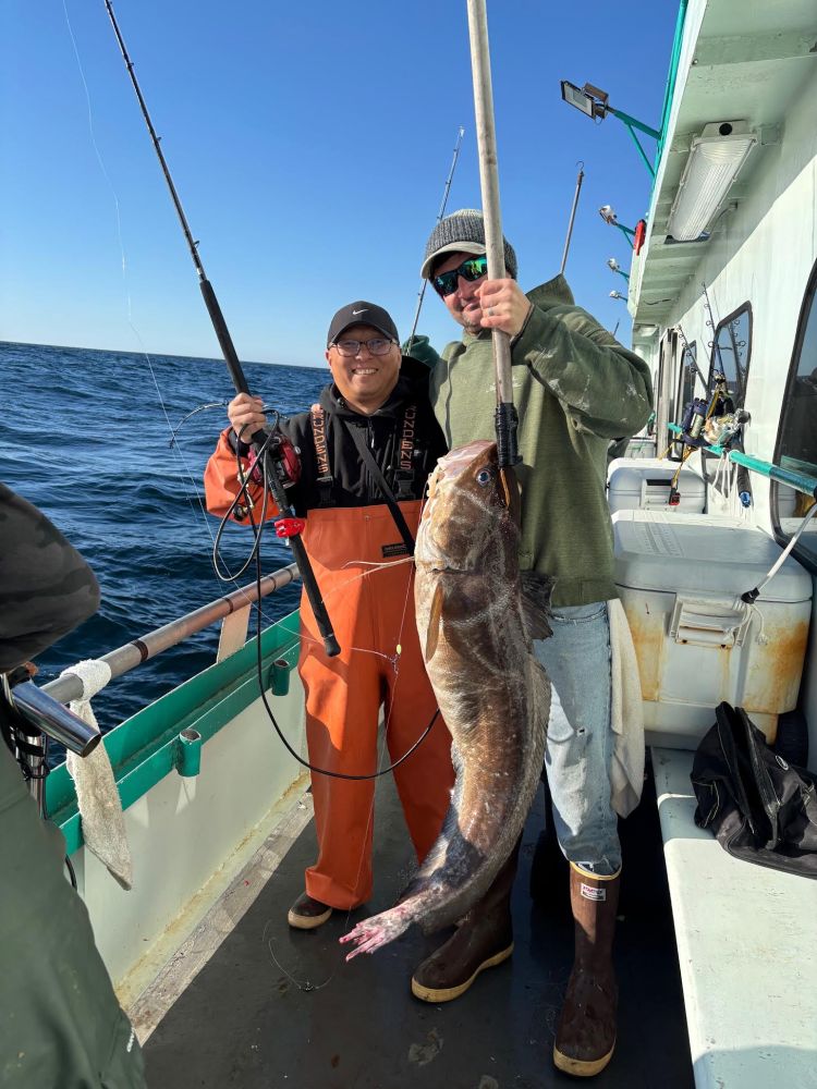 Two people on a boat holding a large fish and fishing rods.