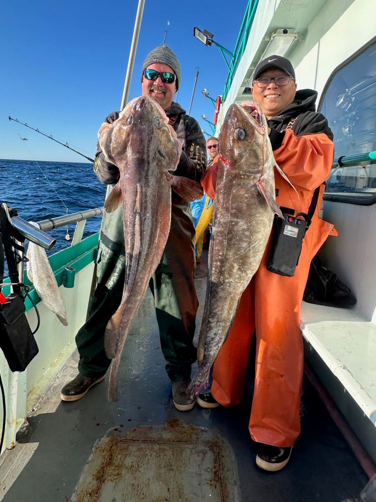 Two people on a boat holding large fish, smiling.