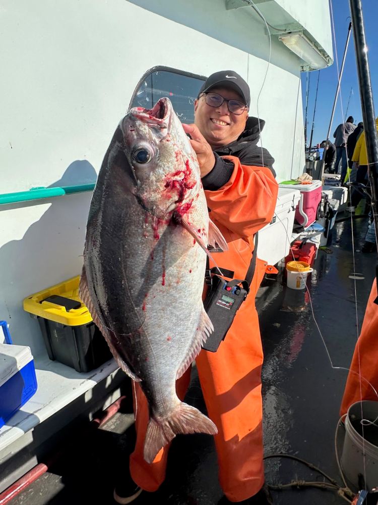 Person in orange gear holding a large, freshly caught fish on a boat deck.