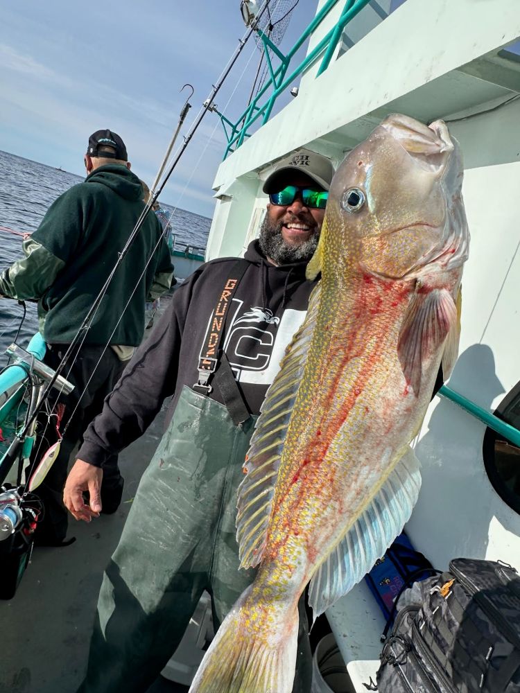 Man holding large fish on a boat with fishing gear visible.