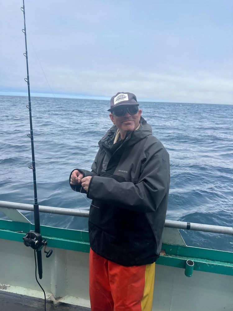 Person in jacket and cap holding fishing line on boat at sea.