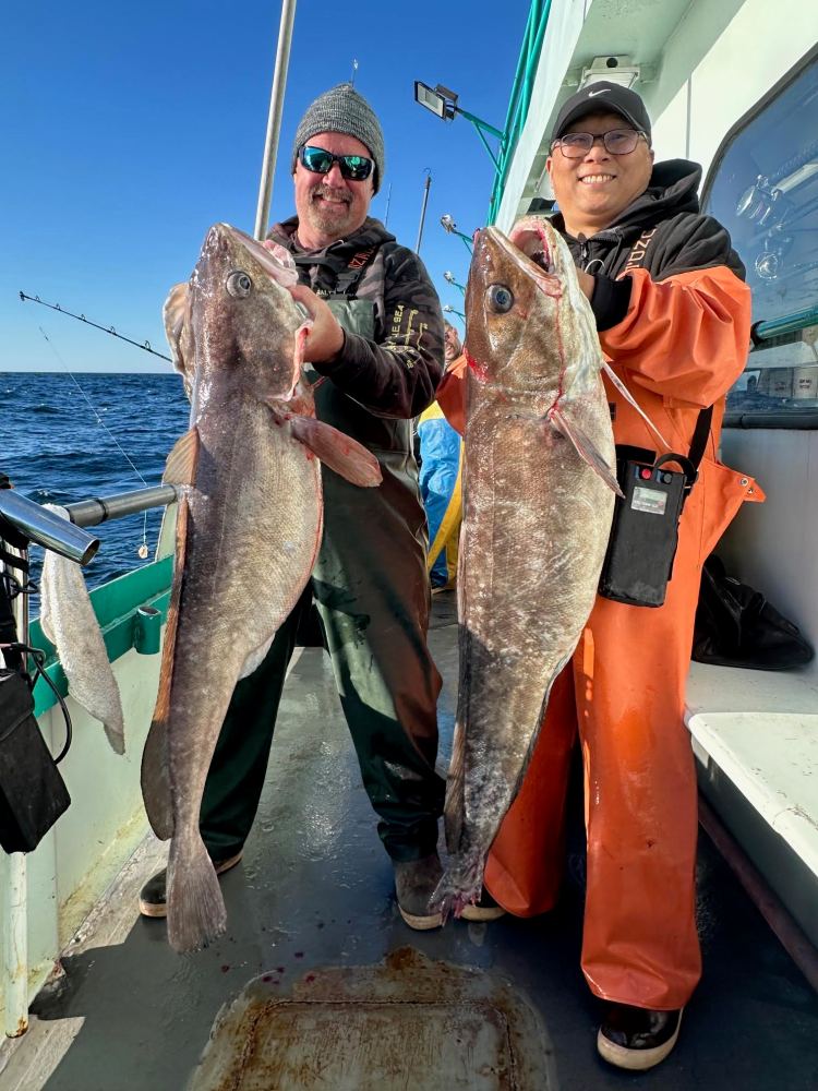 Two people on a boat proudly holding large fish.