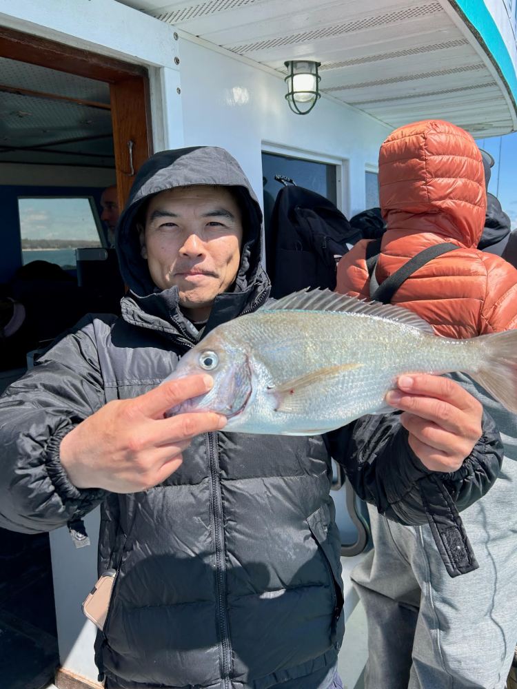 Person in dark jacket holding a large fish on a boat deck.
