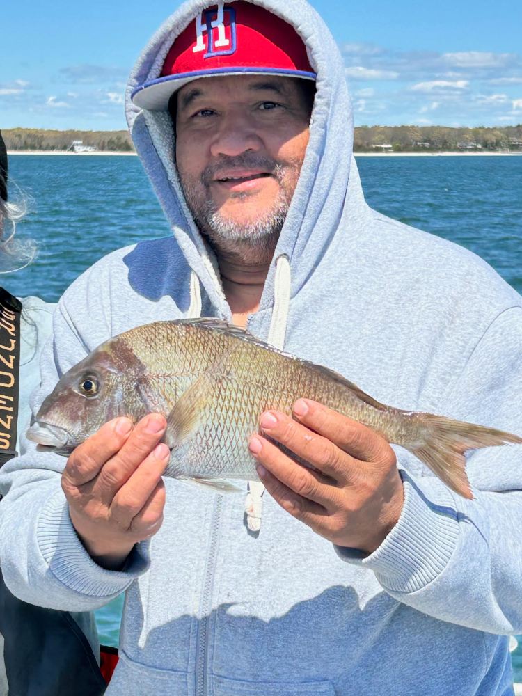 Person in gray hoodie holding a fish on a boat with water in the background.