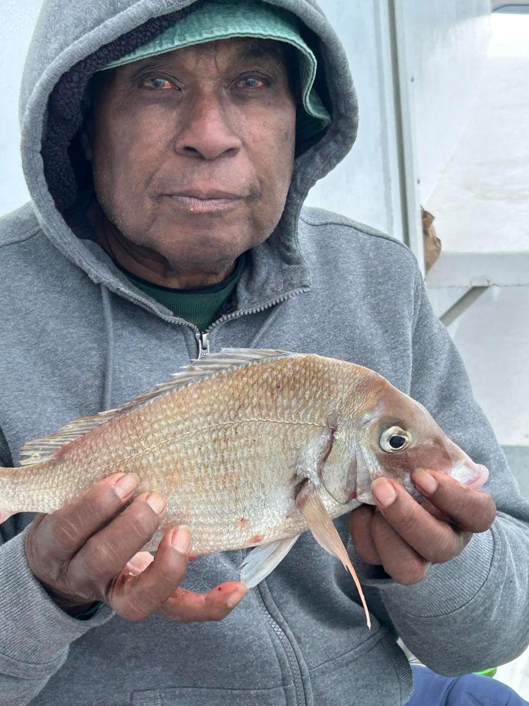 Person in hoodie holding a fish on a boat.