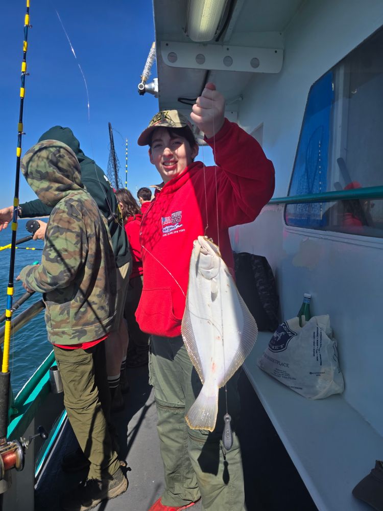 Person in red hoodie holding a fish on a boat under a clear sky.