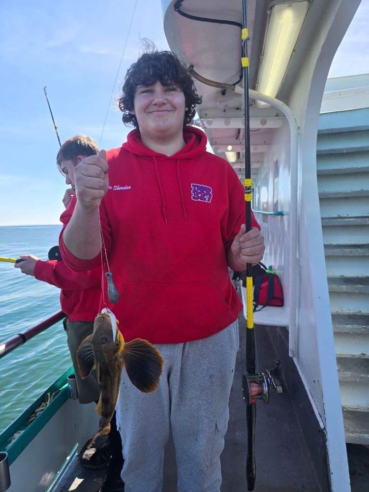 Person in red hoodie holding a fishing rod with a fish on a boat.