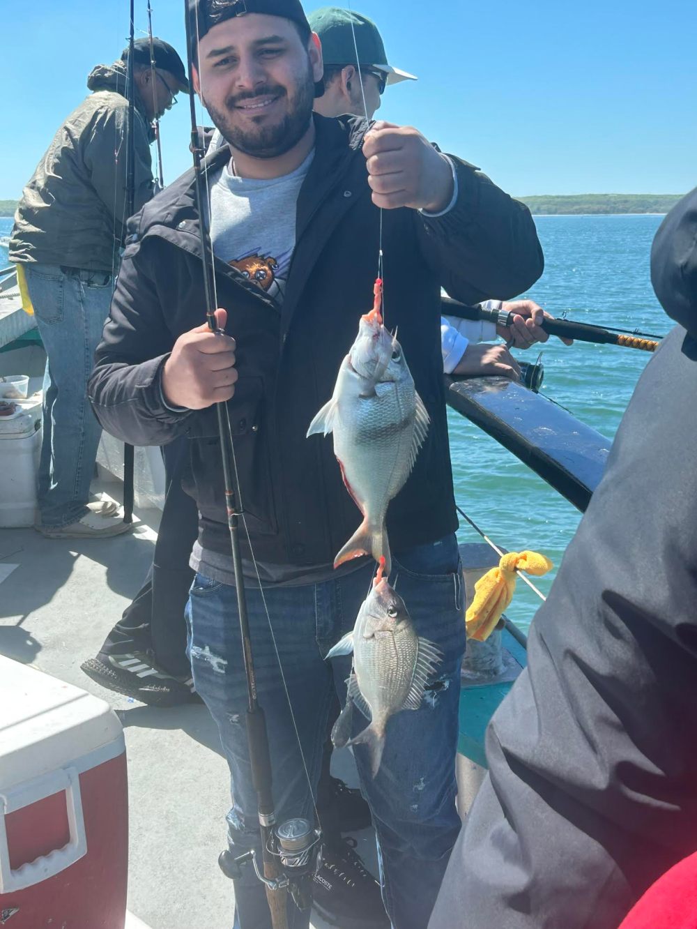 Person holding two fish on a fishing rod on a boat.