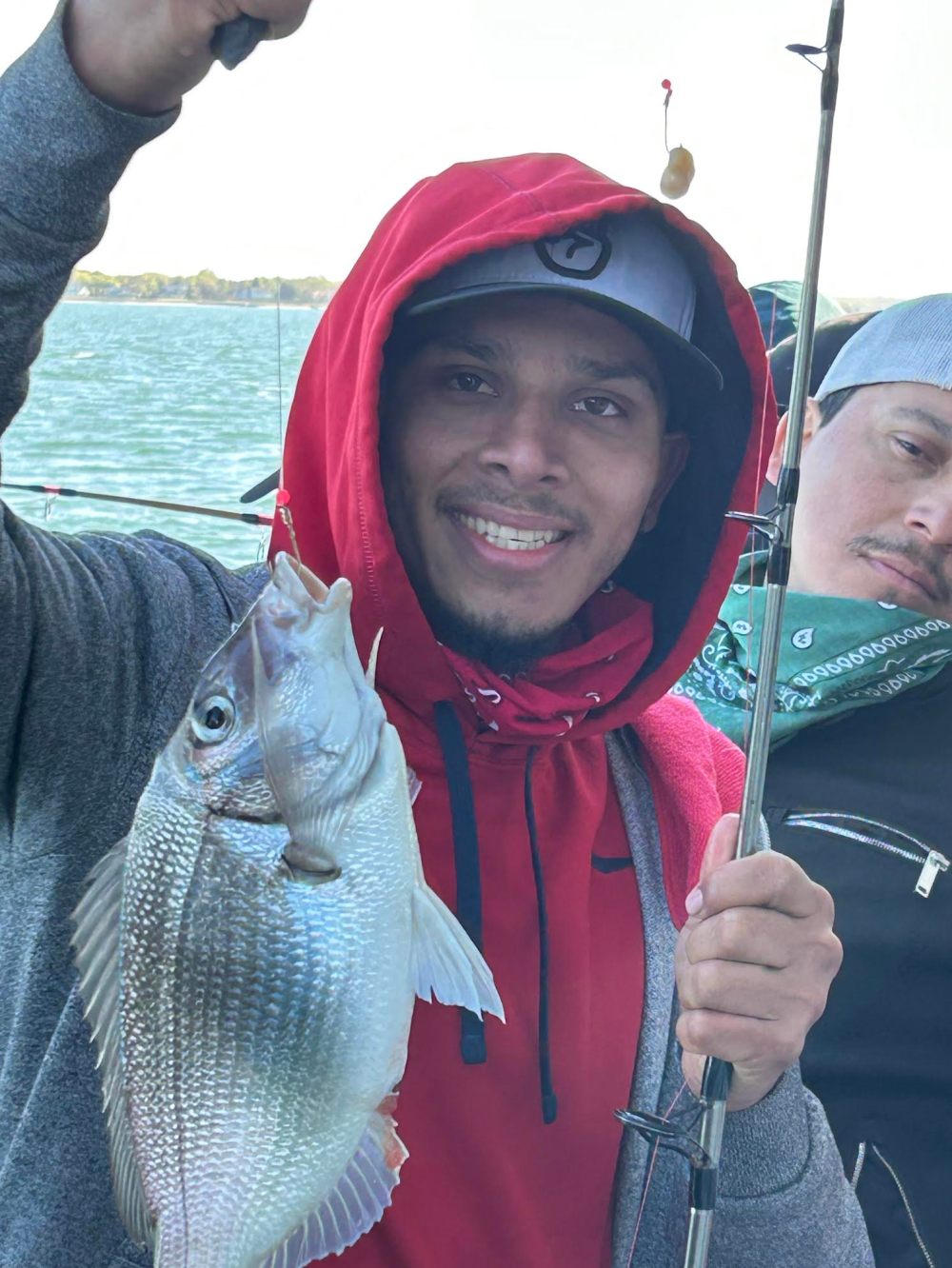 Person in red hoodie holding a fish by a lake.