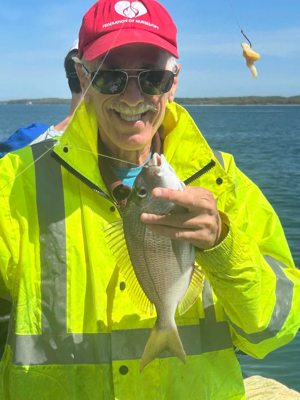Man in yellow raincoat holding a fish and smiling on a boat.