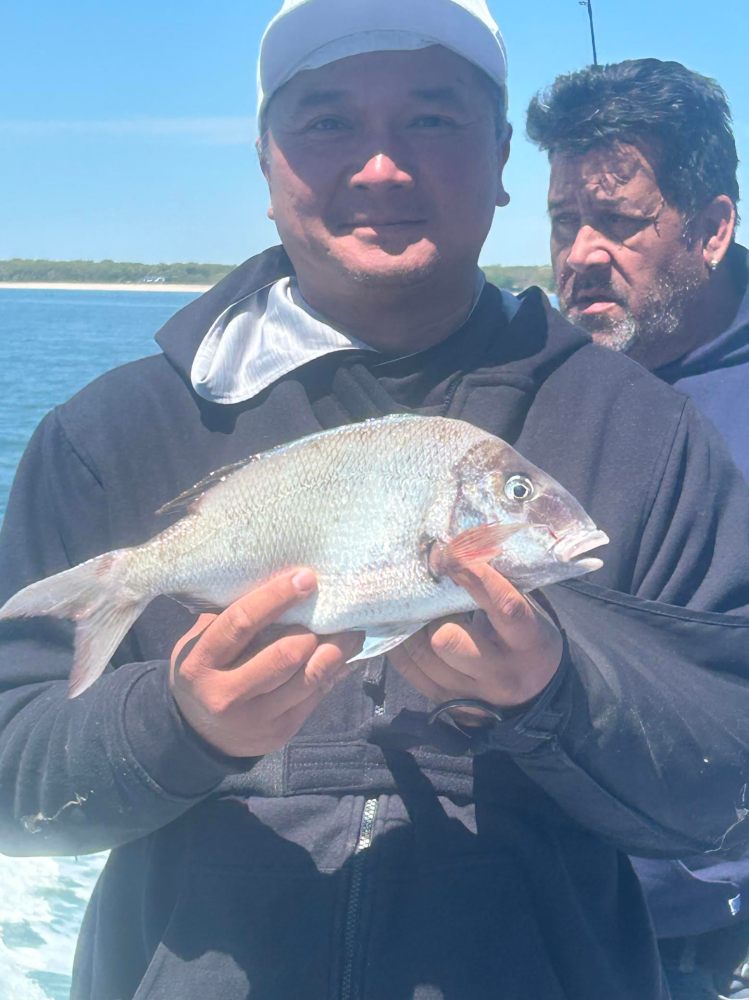 Person holding fish on a boat with another person in the background.
