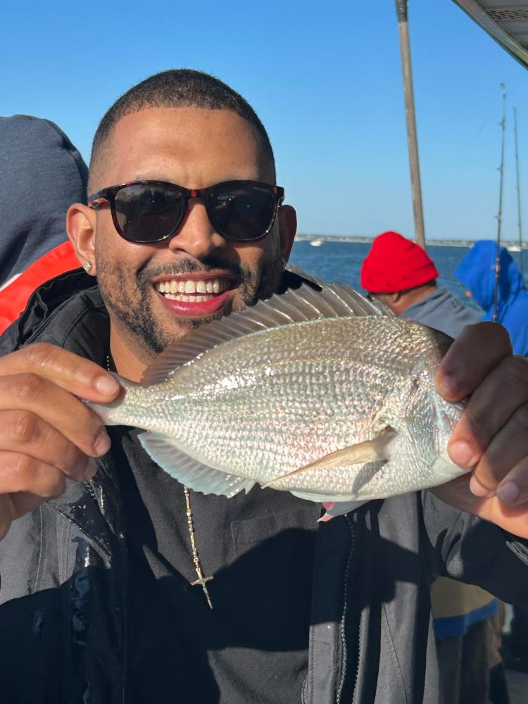Man smiling, holding a fish with both hands near a body of water.