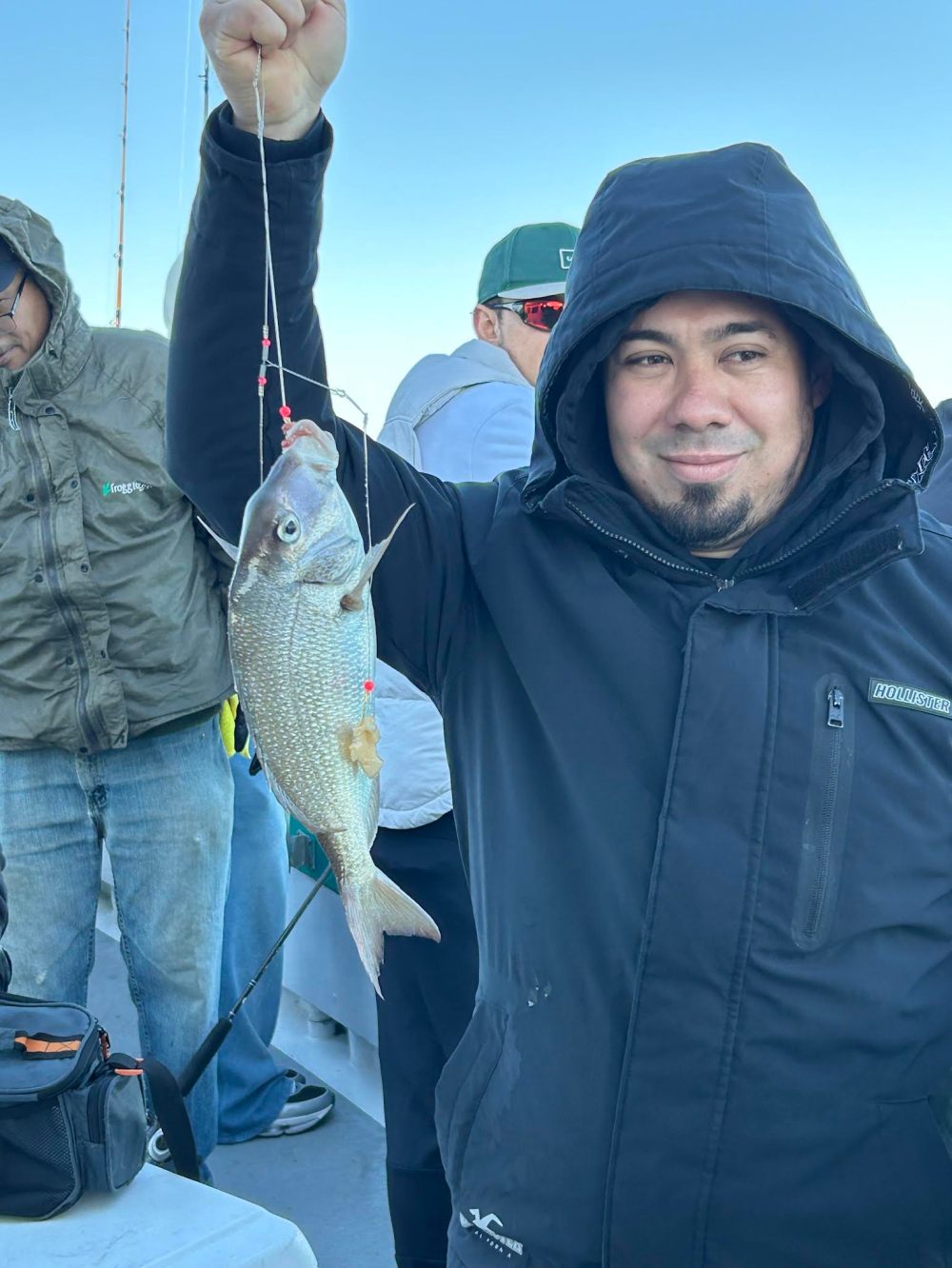 Man in a black jacket holding a fish on a line, with others around on a boat.