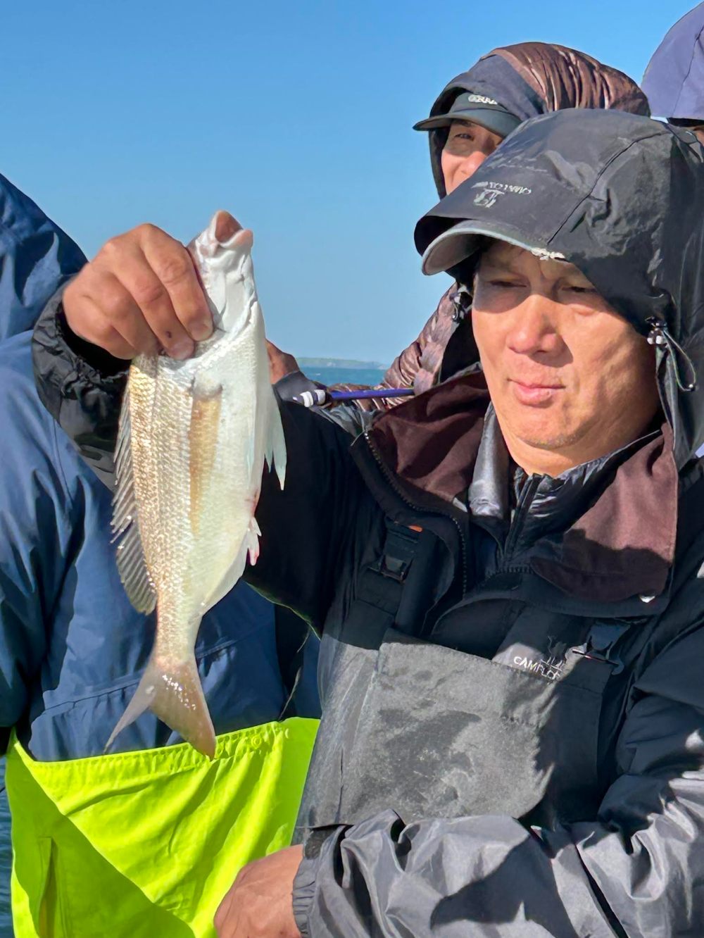 Person in outdoor gear holding a fish on a boat.