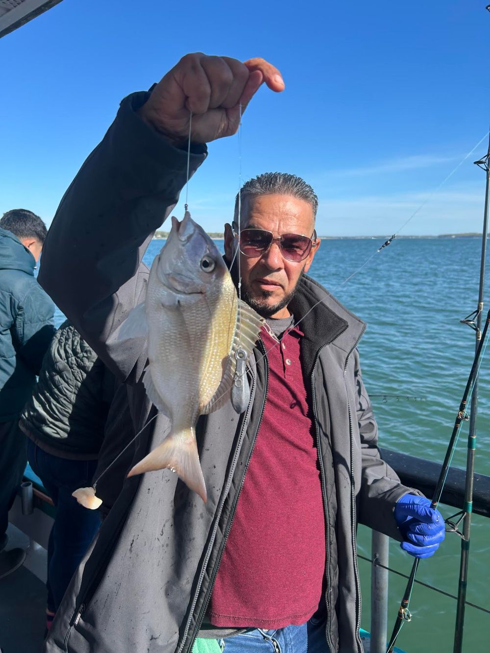 Person on a boat holding a fish, wearing a jacket and gloves.
