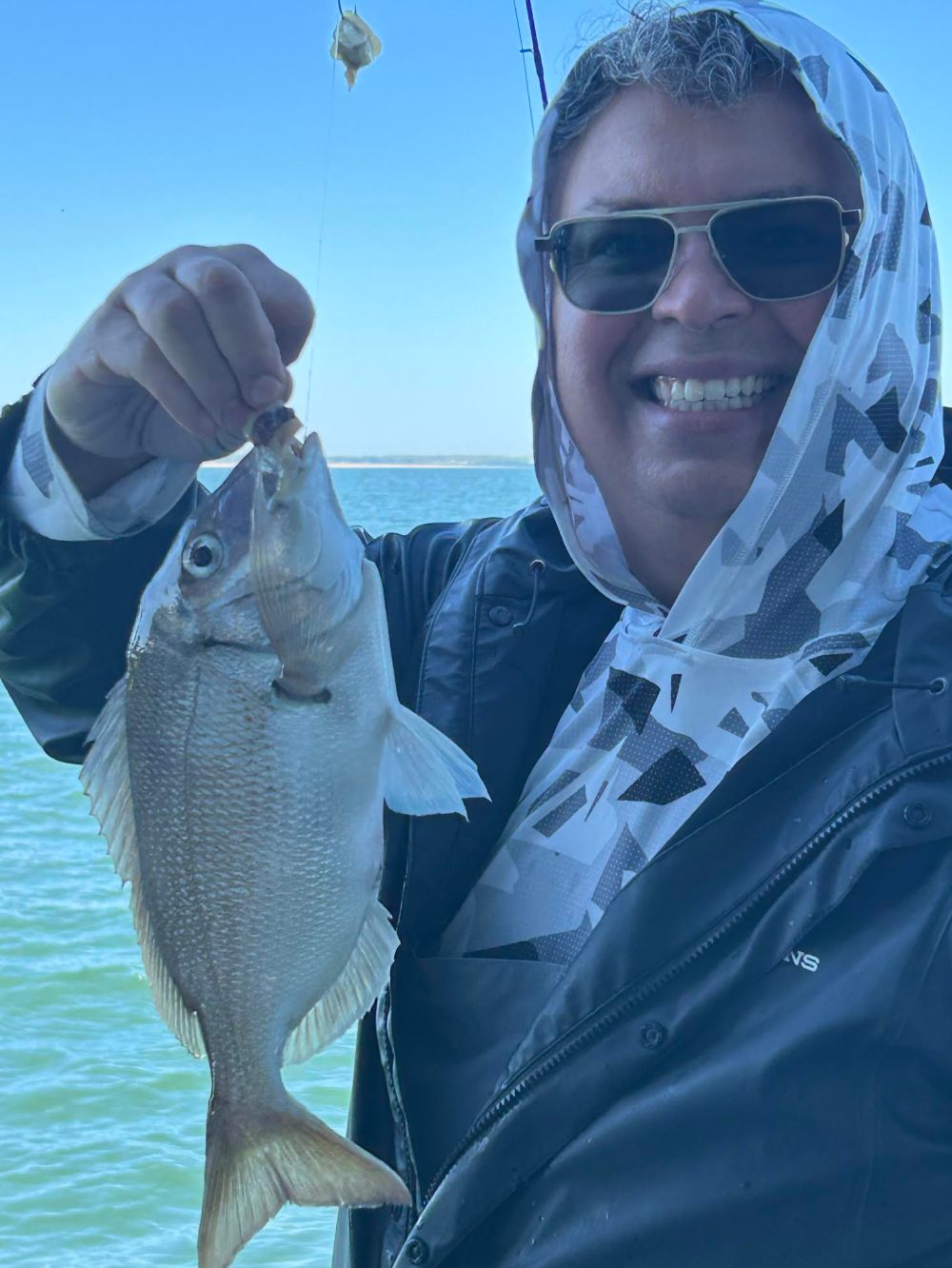 Person holding a fish by the mouth on a sunny day near water.