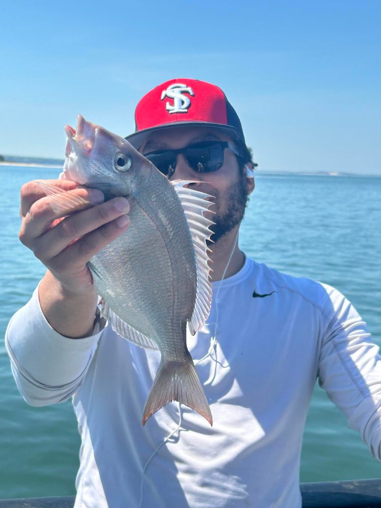 Person holding a fish on a boat with water in the background.