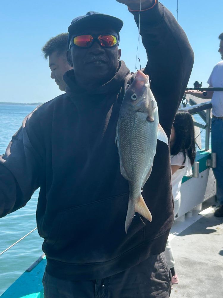 Person on a boat holding a fish by its mouth with others in the background.