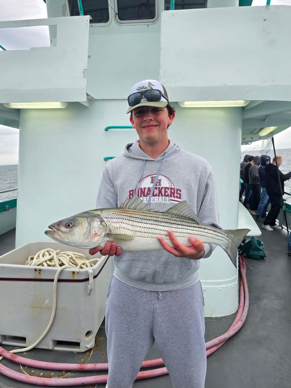 Person holding a fish on a boat wearing a gray hoodie and cap.