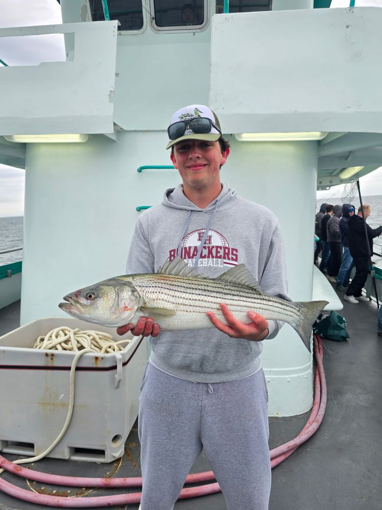 Person holding a large fish on a boat deck, wearing a cap and hoodie.