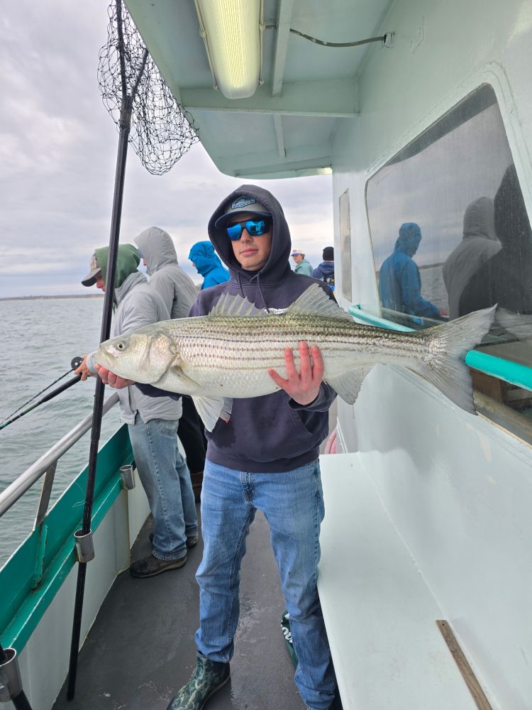 Person in hoodie holding a large fish on a boat with others fishing.