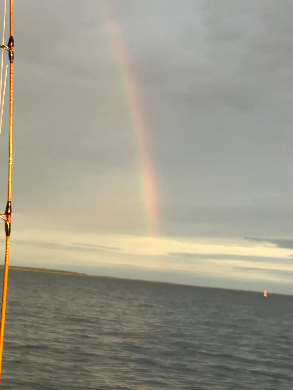 Rainbow over a calm sea under cloudy sky.