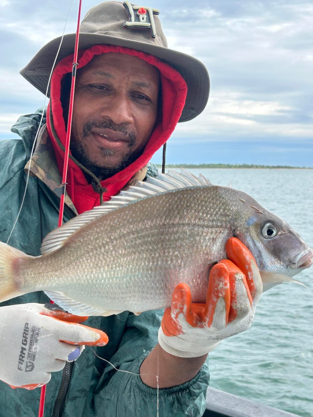 Person holding a large fish with gloved hands on a boat under a cloudy sky.
