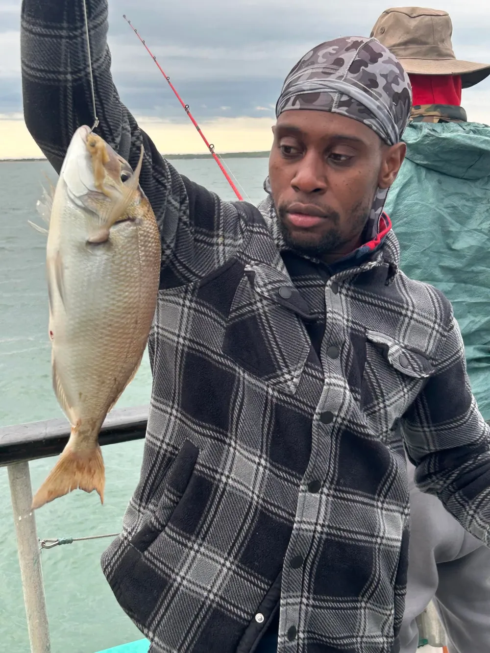 Person holding a fish on a boat with overcast sky.