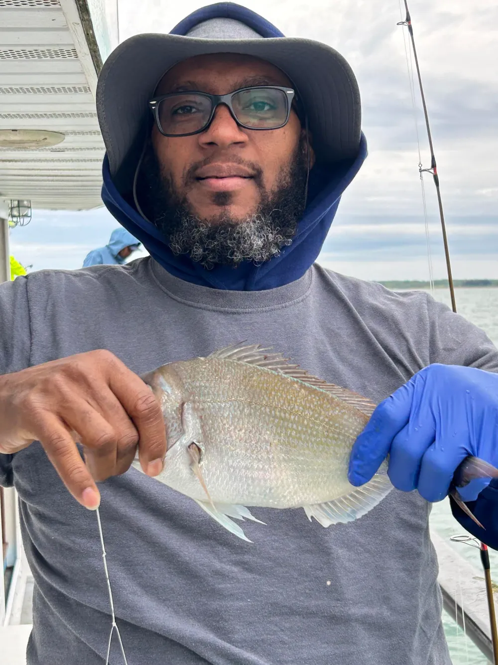 Man wearing a hat and gloves holding a fish on a boat.
