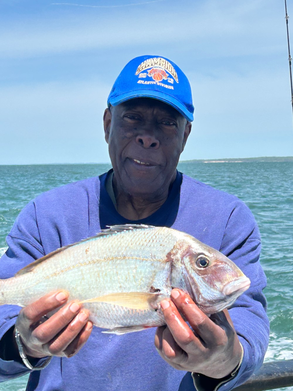 Person in blue shirt holds a large fish on a boat with ocean in the background.