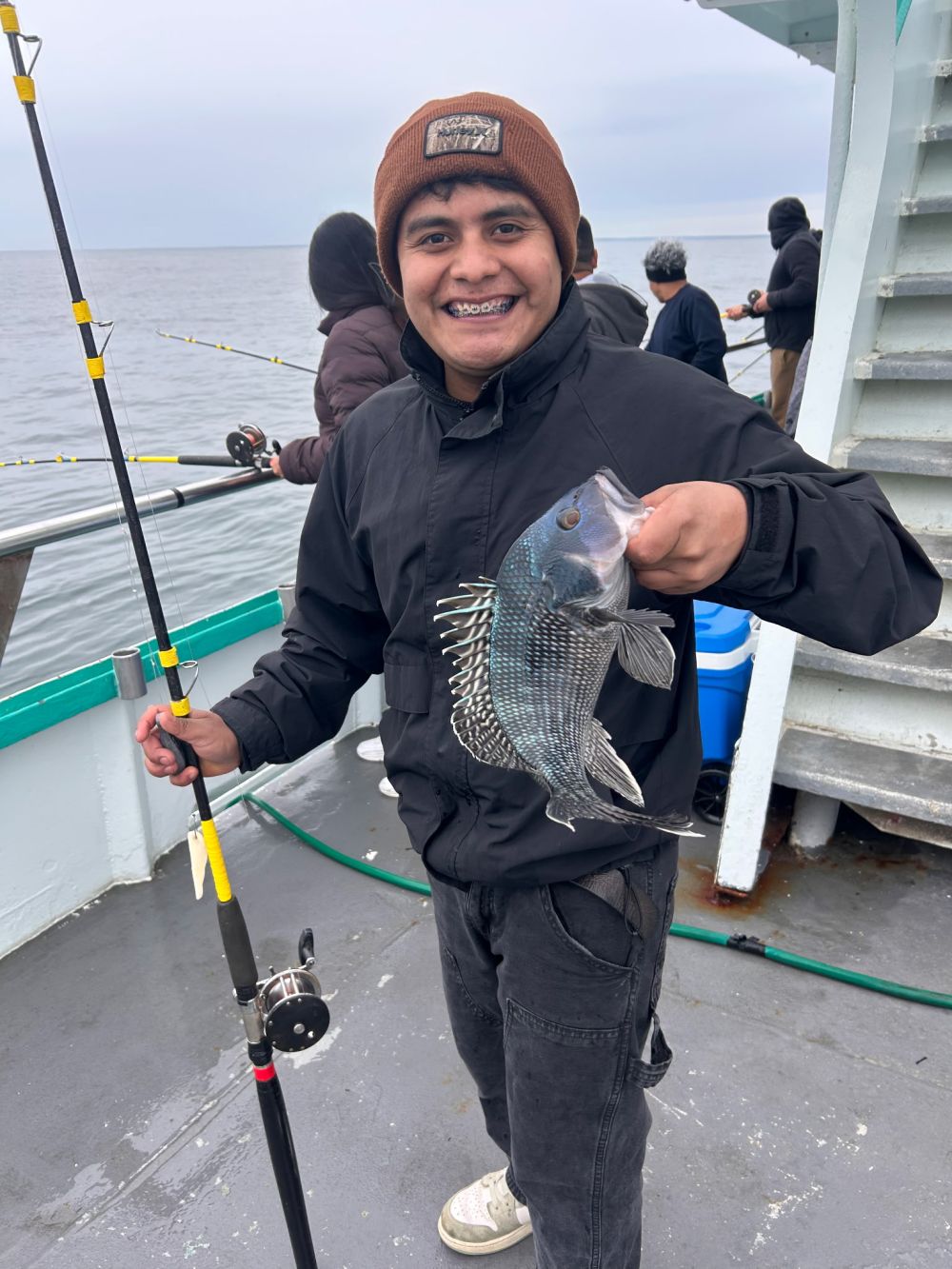 Person on boat holding a fish, smiling, with a fishing rod.