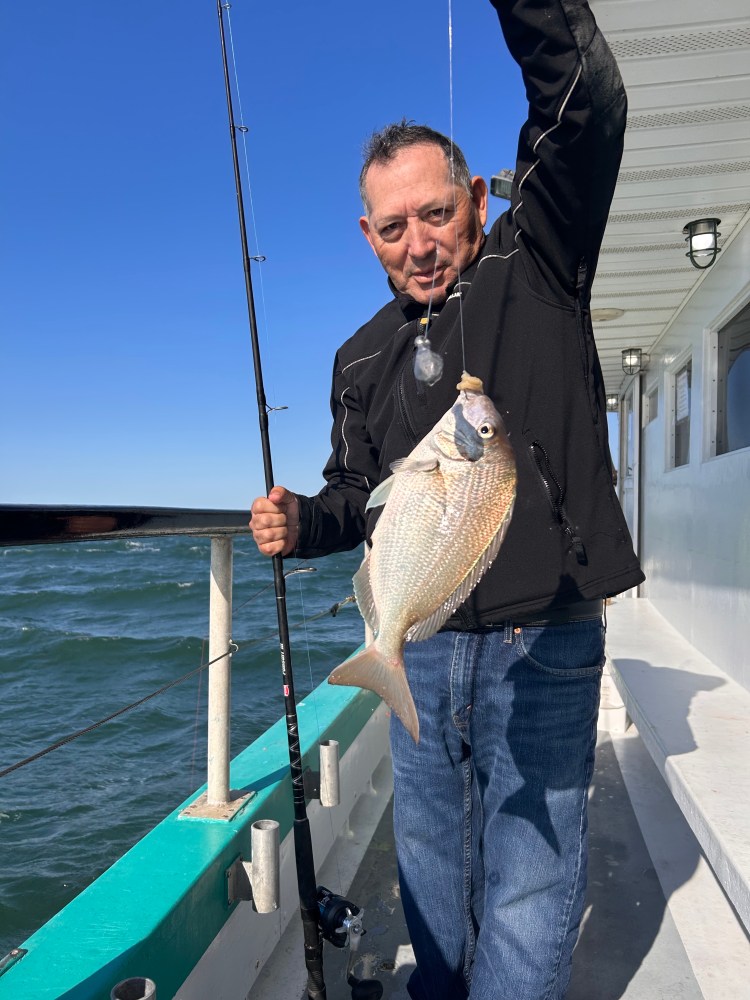 Man holding a fishing rod and a fish on a boat deck.