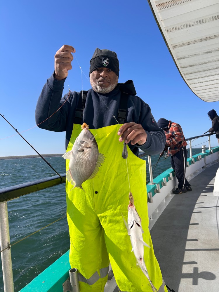 Person in yellow overalls holding two caught fish on a boat.