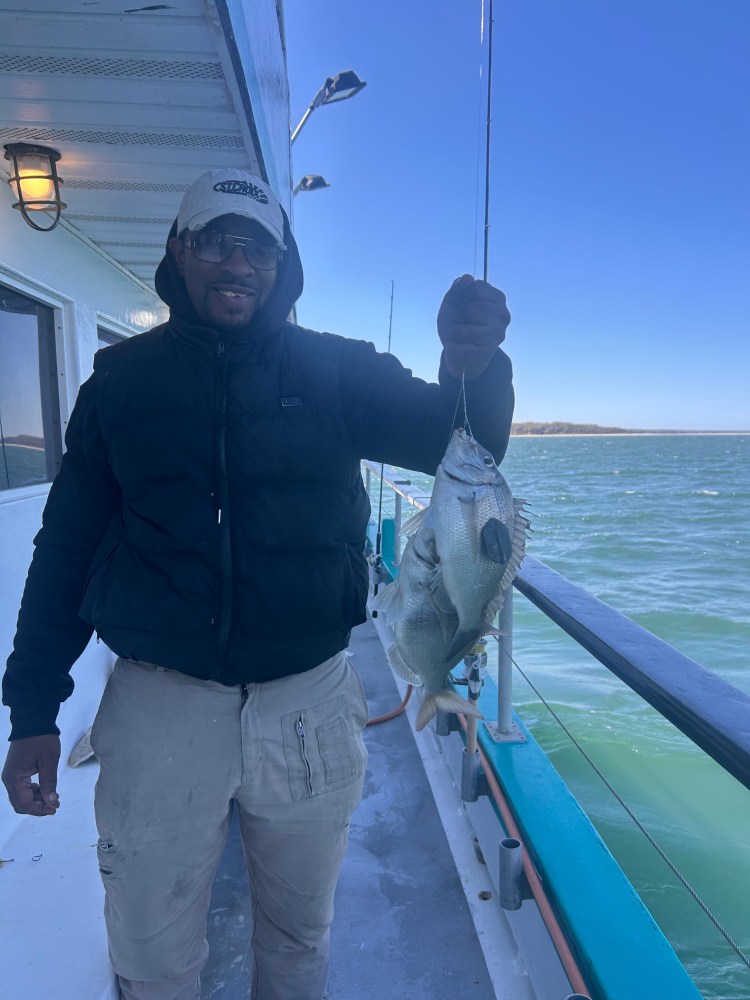 Person holding a fish on a boat with water in the background.