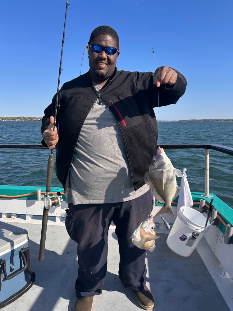 Man holding fishing rod and fish on a boat under clear blue sky.