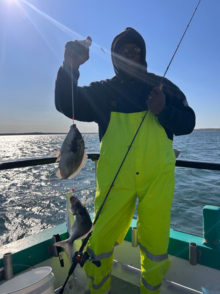 Person in yellow overalls holds up two fish on a boat.