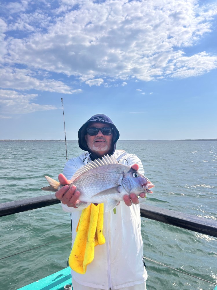 Person in white jacket holding a large fish on a boat with a cloudy sky.