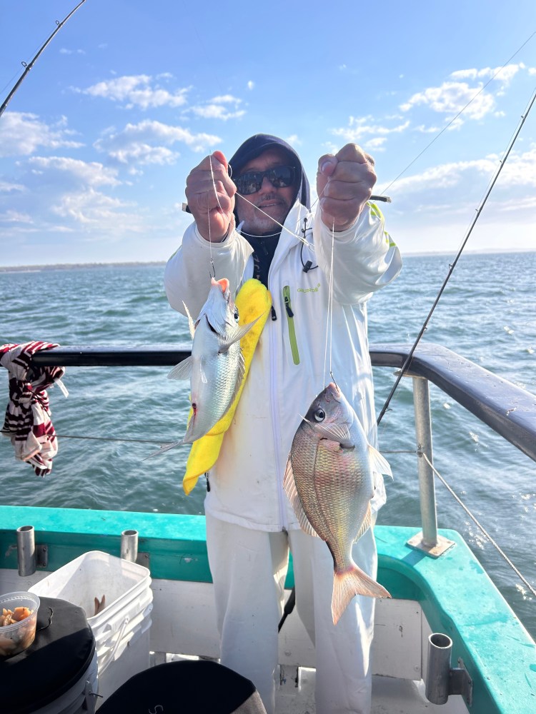 Person on boat holding two fish, one yellow, under a clear sky.