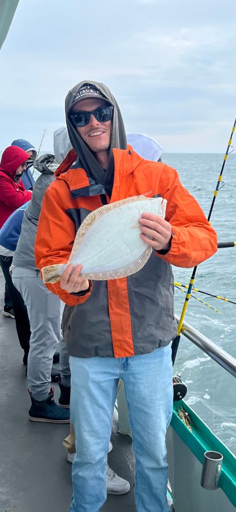 Person on a boat holding a flat fish, wearing an orange and gray jacket.