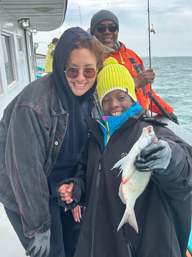 Three people on a boat, child holding a fish, smiling.