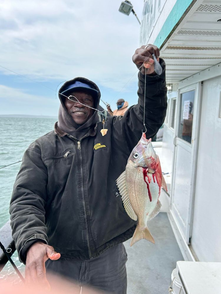 Person holding a fish on a boat, smiling at the camera.